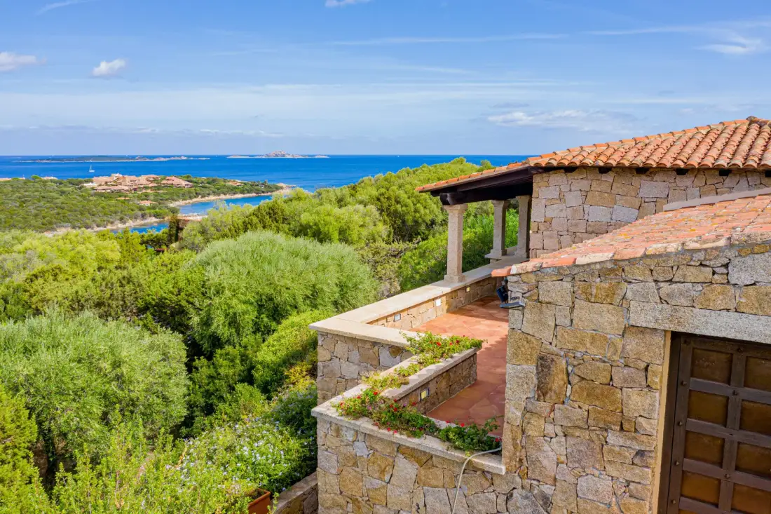 A stone building overlooks green coastal vegetation and the blue sea.