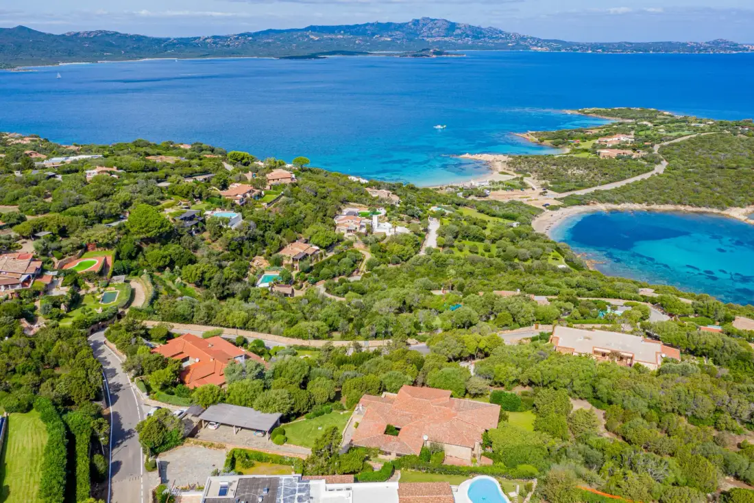 An aerial view of a coastal settlement, with green hills beside a bright blue bay.