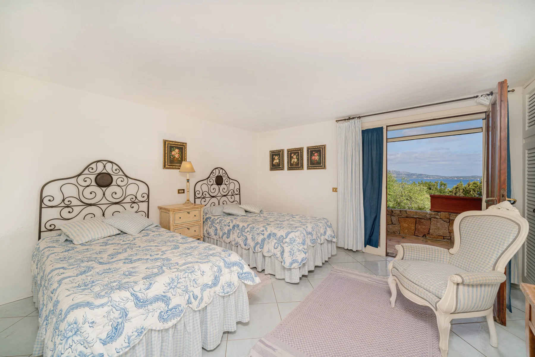 A bedroom with two beds, patterned bedding, and a seating area by the window.