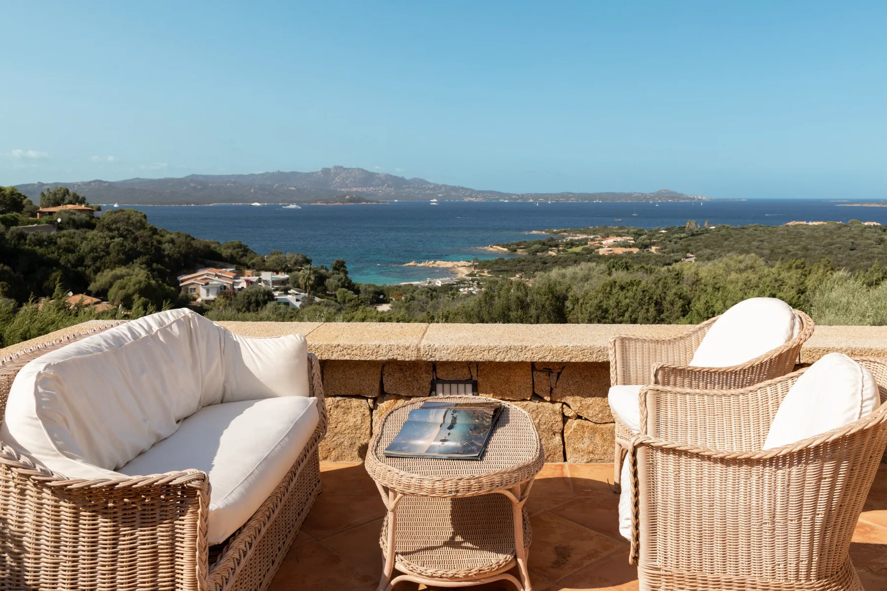 A terrace seating area overlooks the sea and a green coastline.