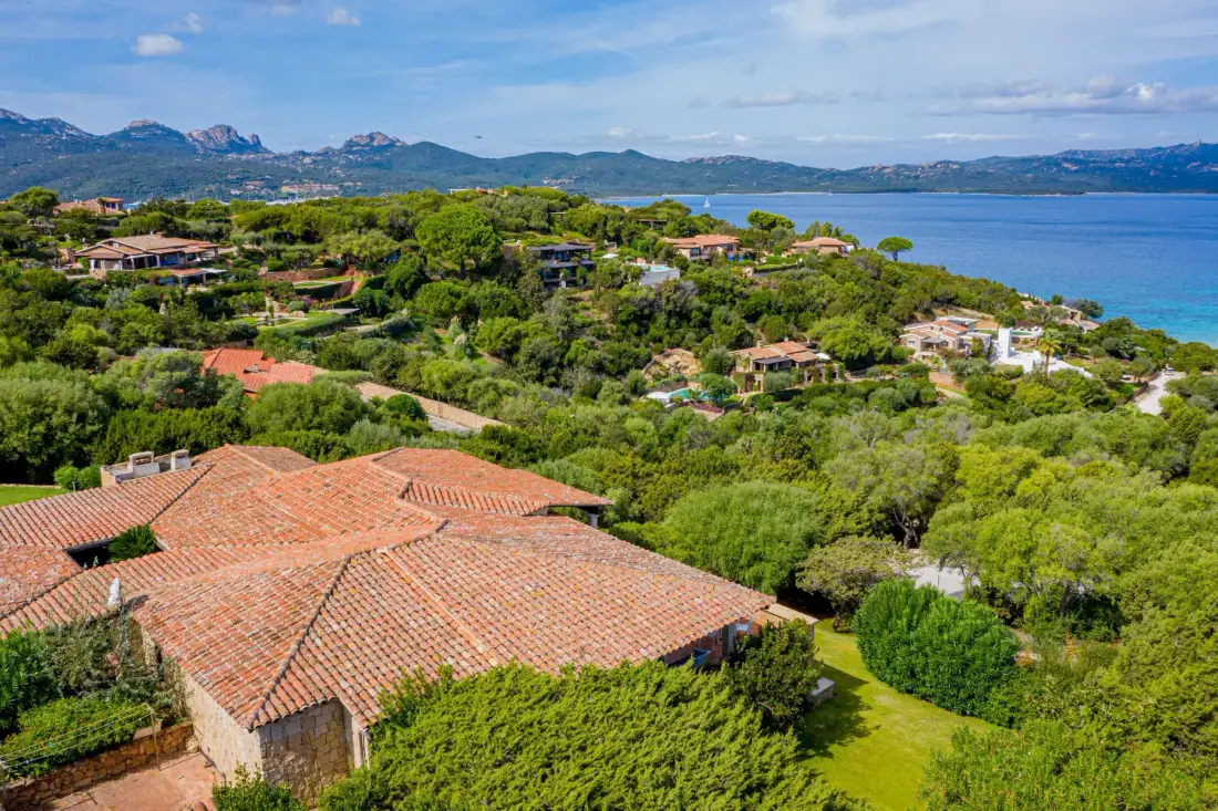 Aerial view of terracotta-roofed homes among green hills beside the water.
