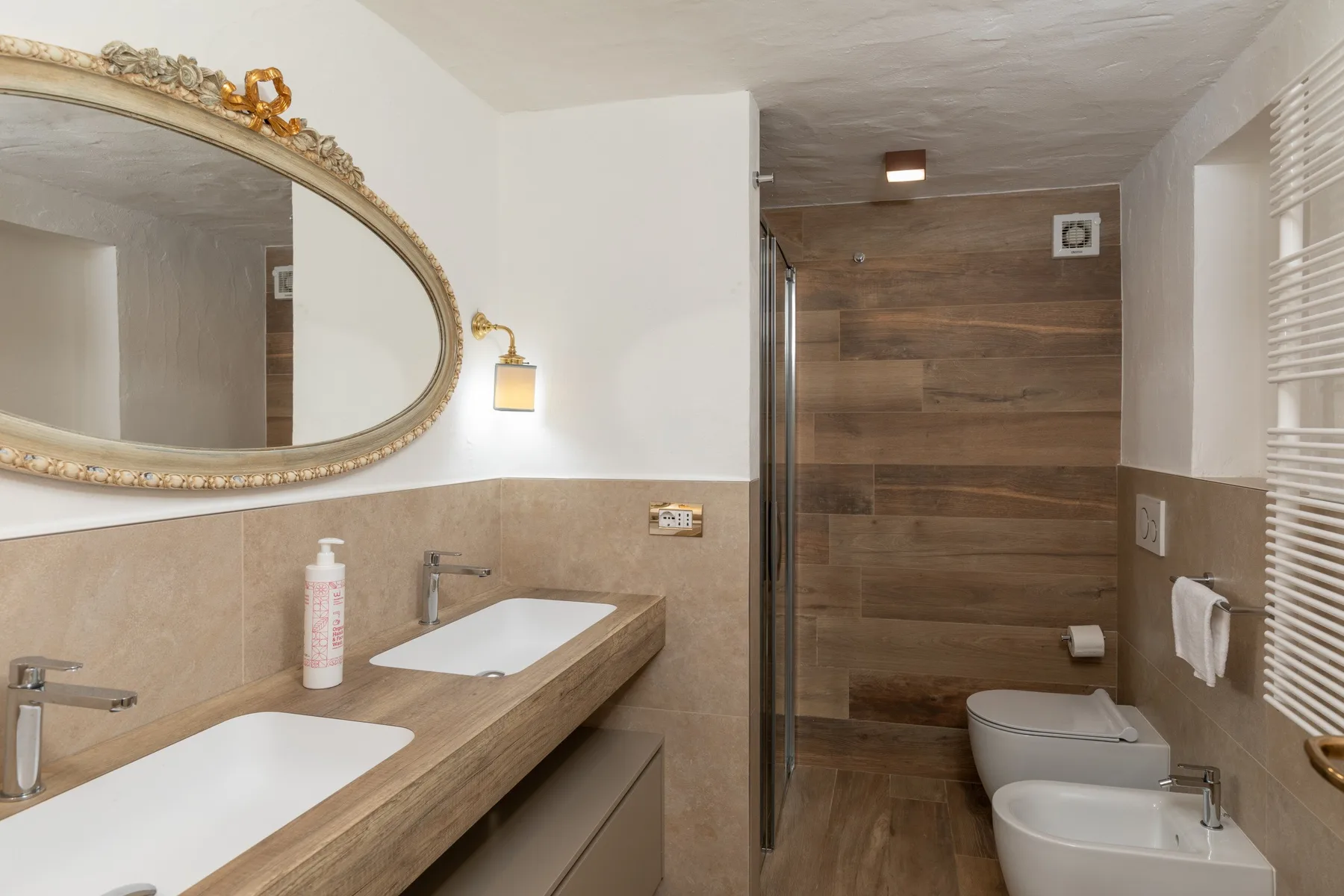 A bathroom with a long vanity, large oval mirror, and walk-in shower.