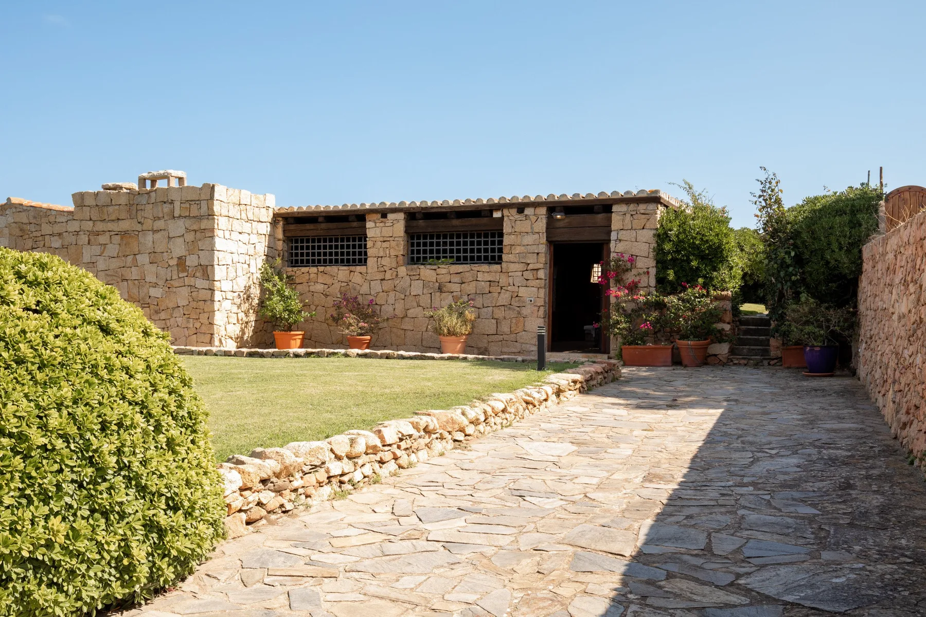 A stone courtyard with a paved path, a small lawn, and a low stone building.