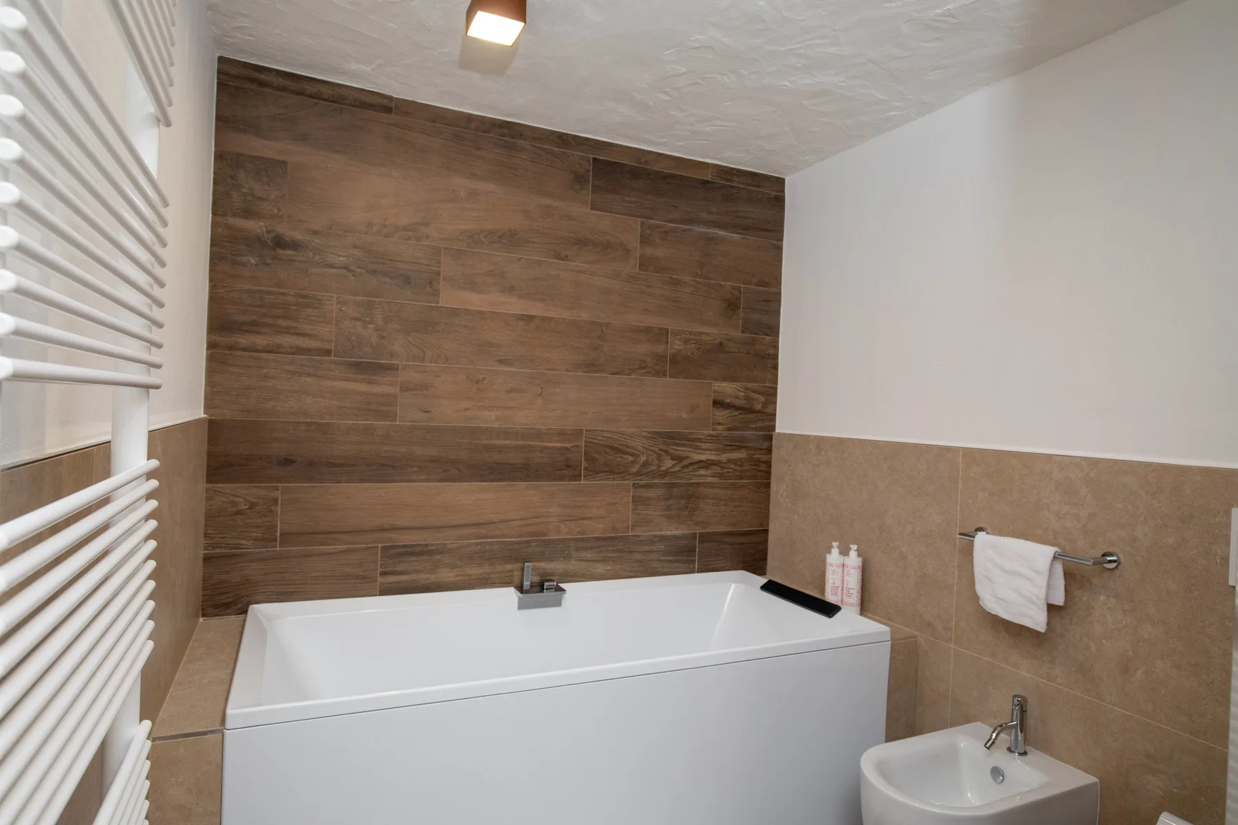 A bathroom with a bathtub and wood-look tiled wall.