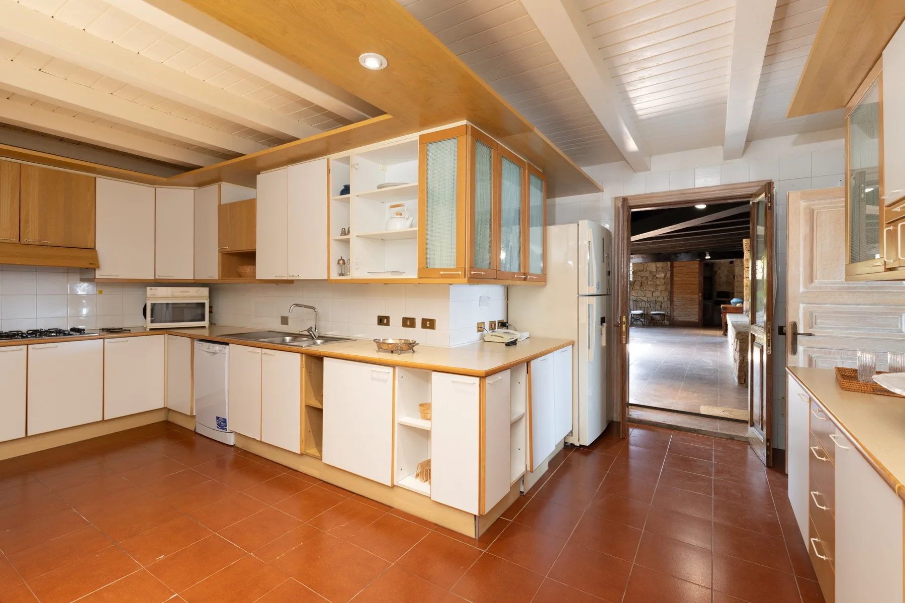 A kitchen with light cabinetry, a central counter, and terracotta-colored floor tiles.