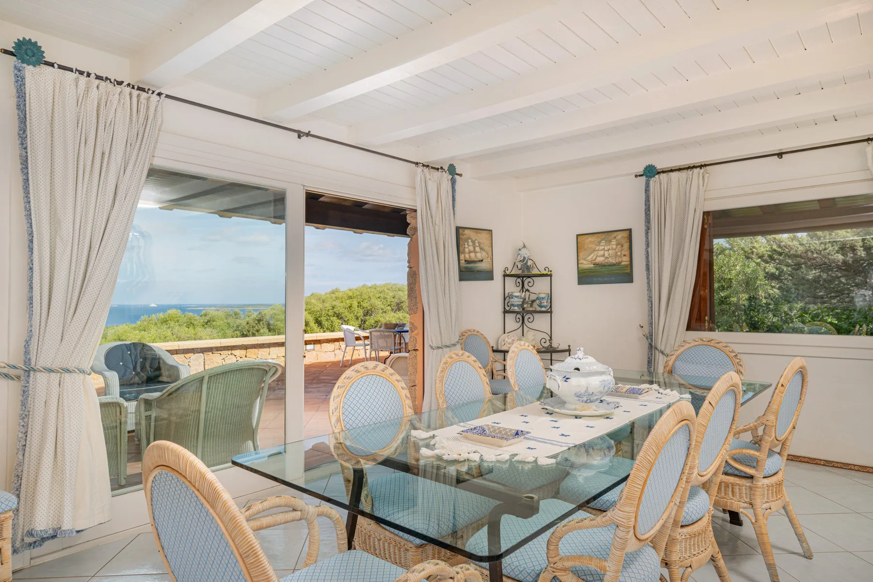 A bright dining area with a glass table and wicker seating beside open views.