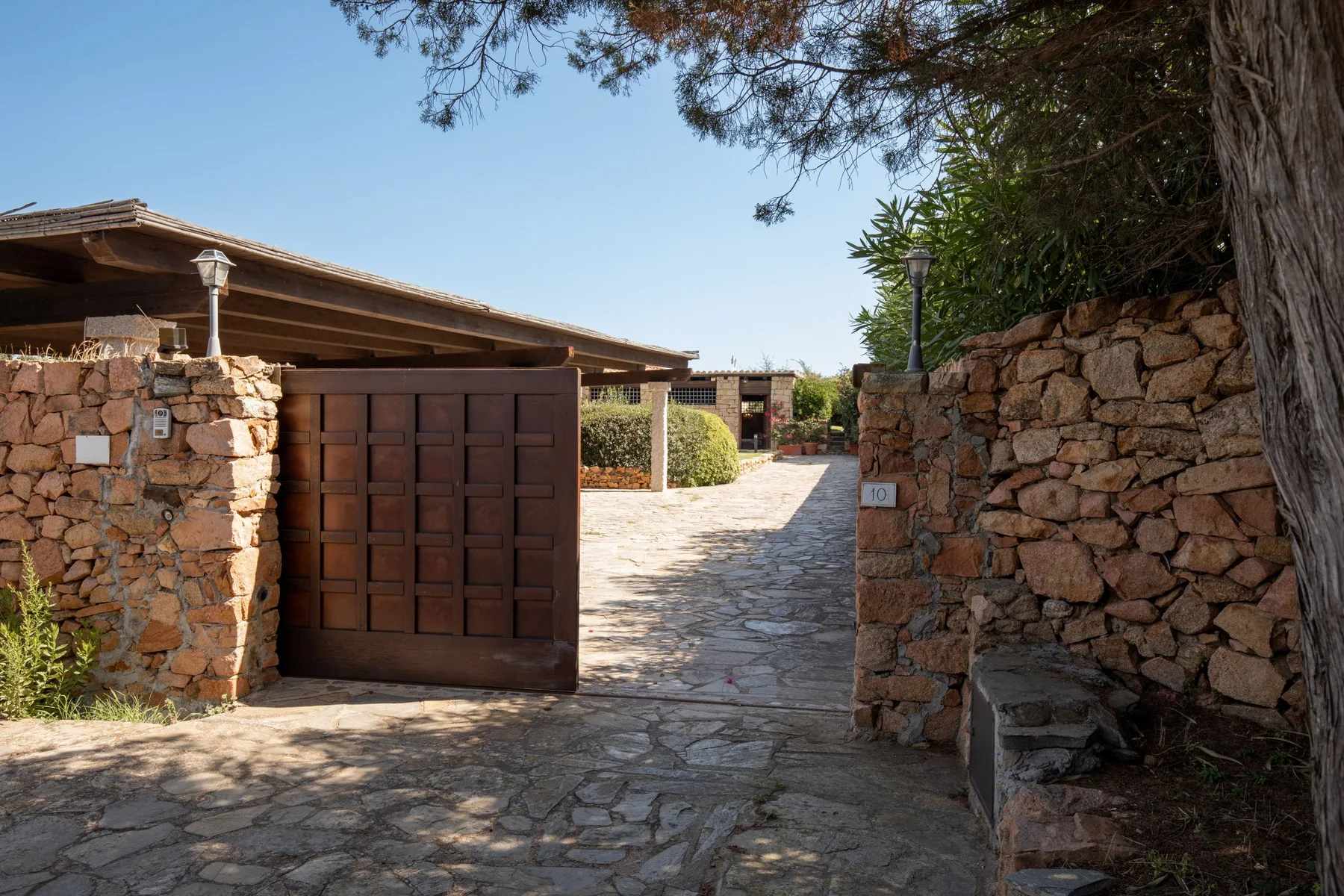 A stone-paved entrance path passes between stone walls and an open wooden gate.