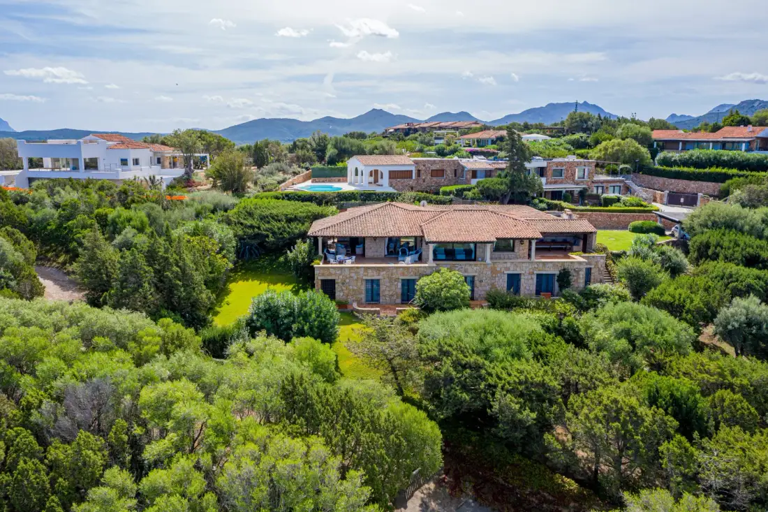 A residential area with houses among greenery and hills in the distance.