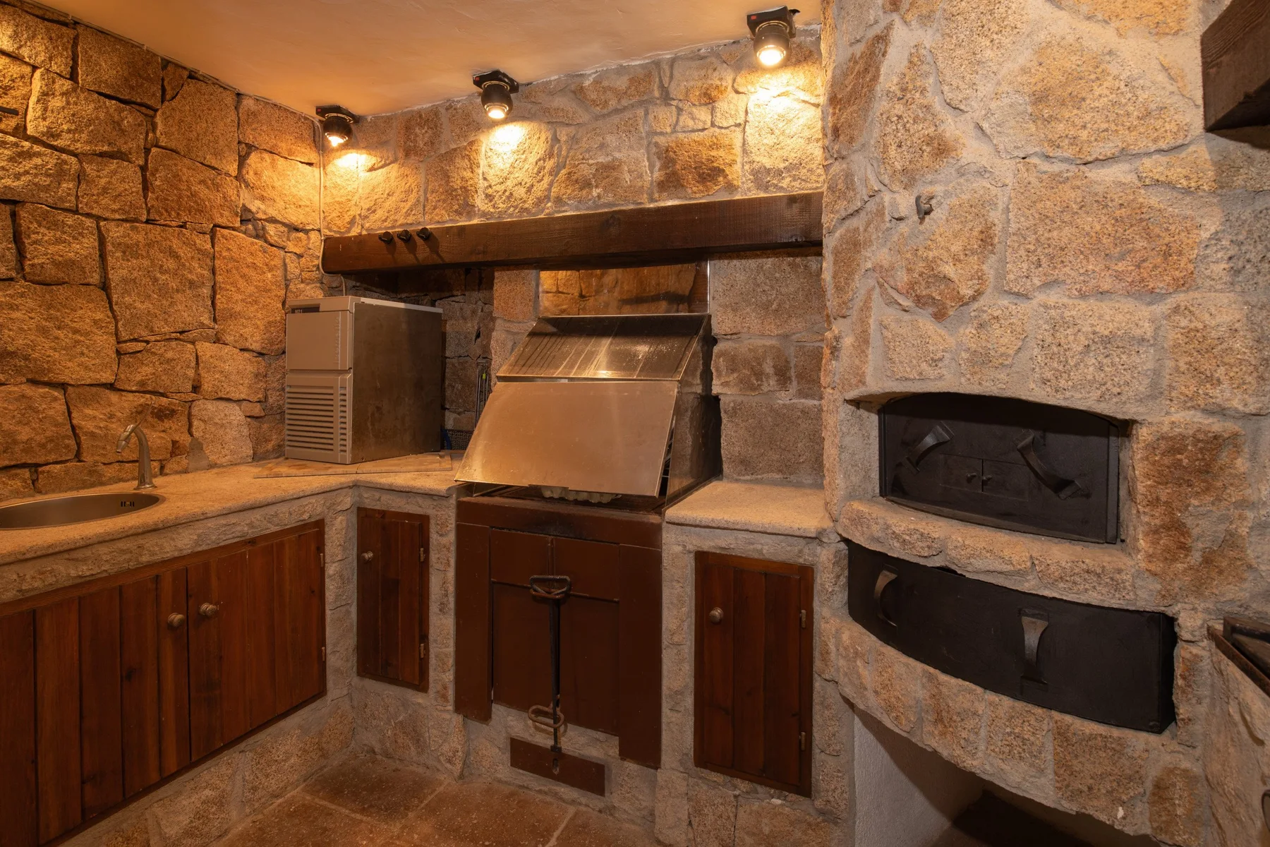 A stone-walled kitchen with wooden cabinets and a built-in grill.