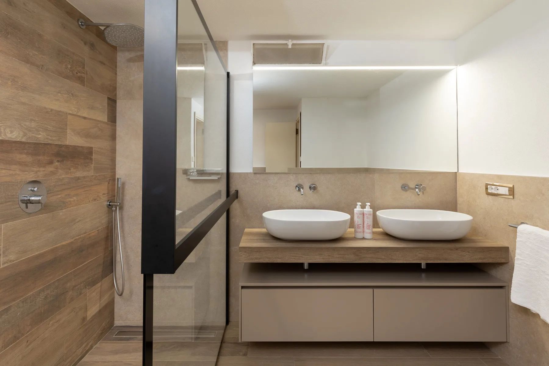 A bathroom with a walk-in shower and a double vanity beneath a wide mirror.