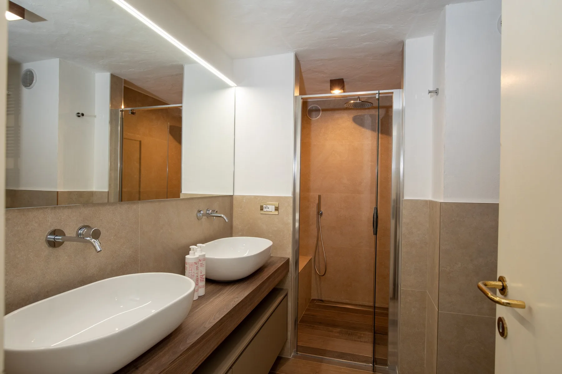 A bathroom with a long vanity, two basins, and a glass shower.