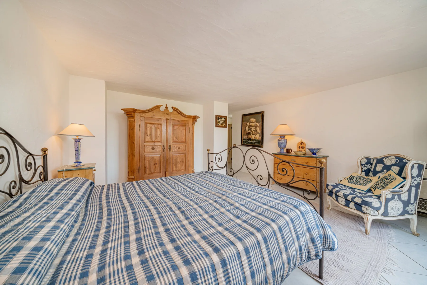 A bedroom with a large bed, wooden wardrobe, and patterned seating.