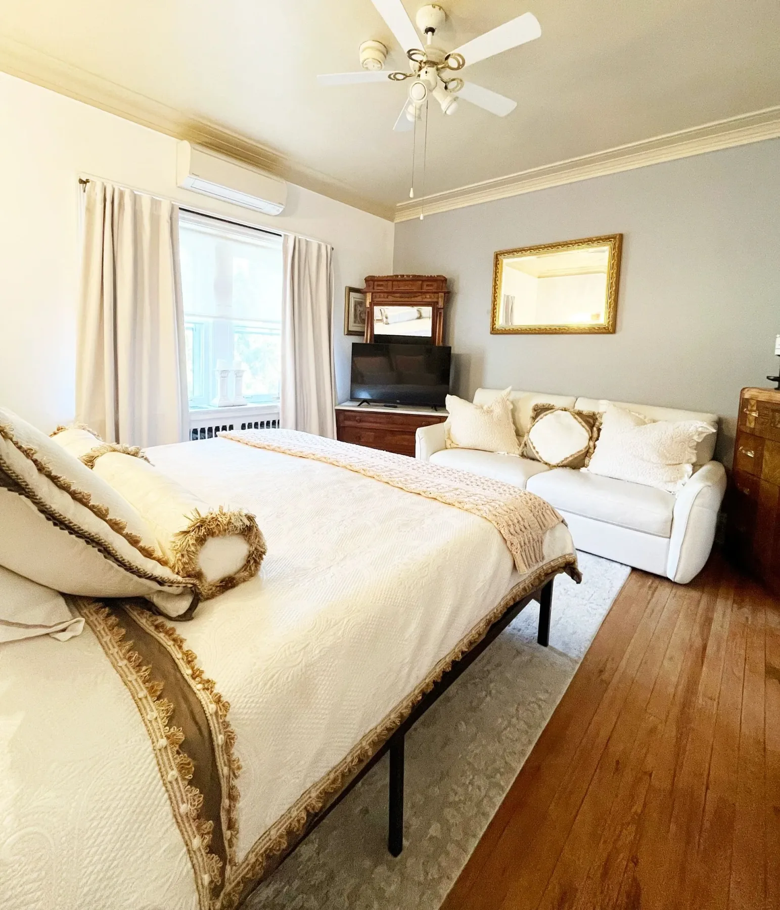 Dormitorio luminoso con una cama, un sofá y suelo de madera.