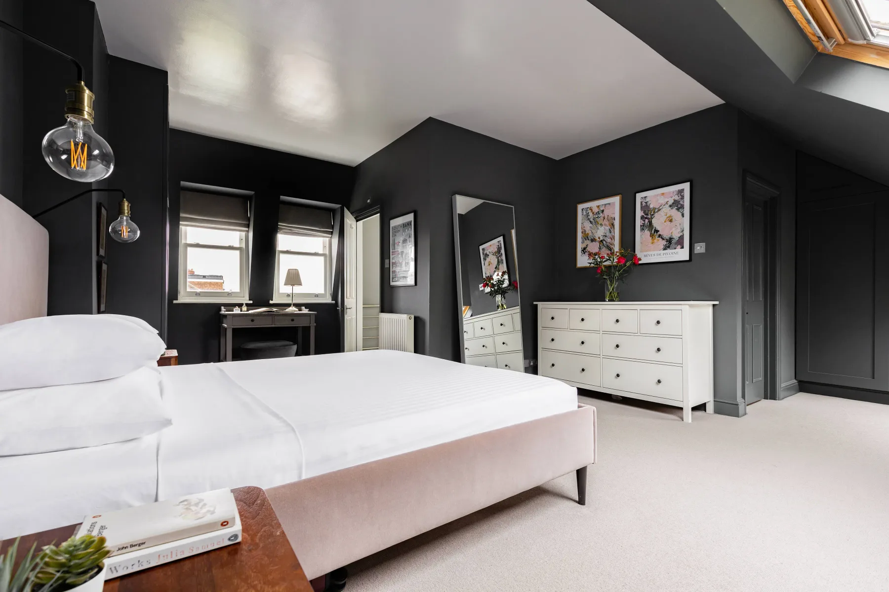 A bedroom with a large bed, a white dresser, and windows.