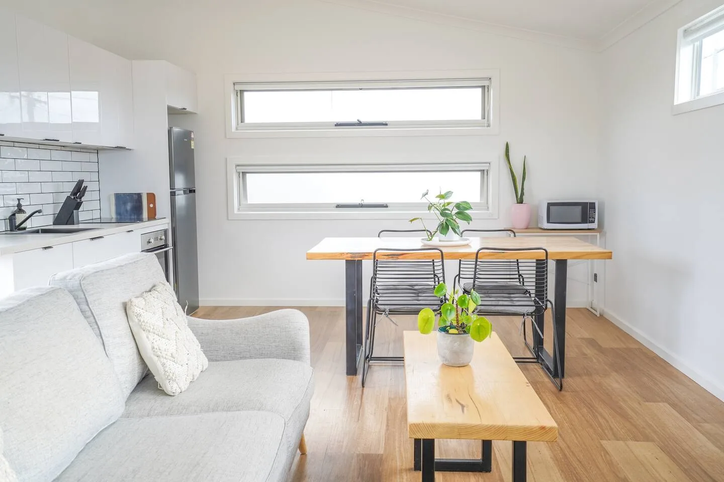 A bright open-plan living and dining area with a kitchen and wooden furniture.