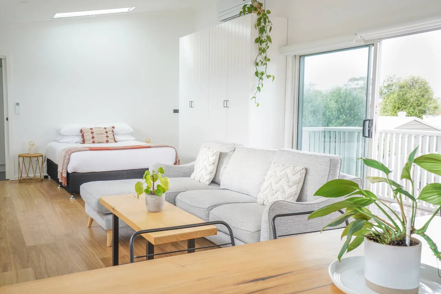 A bright living and sleeping area with a gray sofa and a bed beside the balcony.