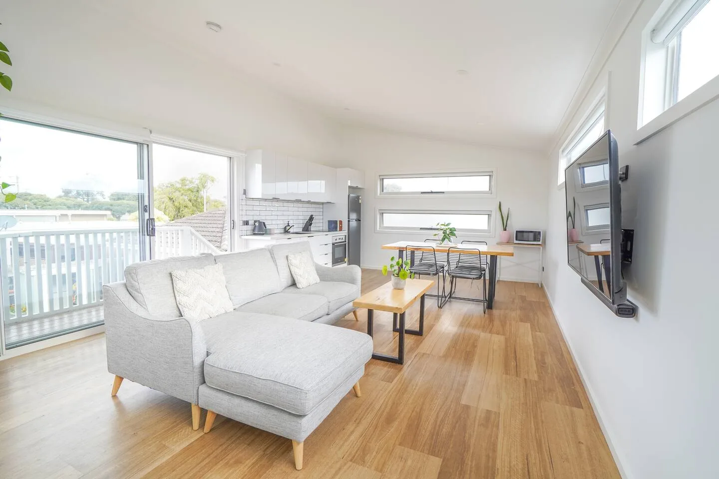A bright open-plan living area has a sectional sofa facing a wall-mounted television.