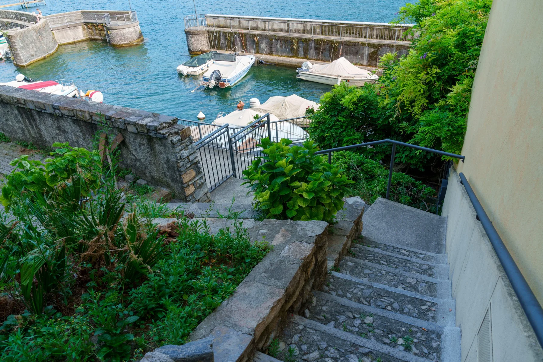 Stone steps descend through greenery toward a small waterfront dock with boats.