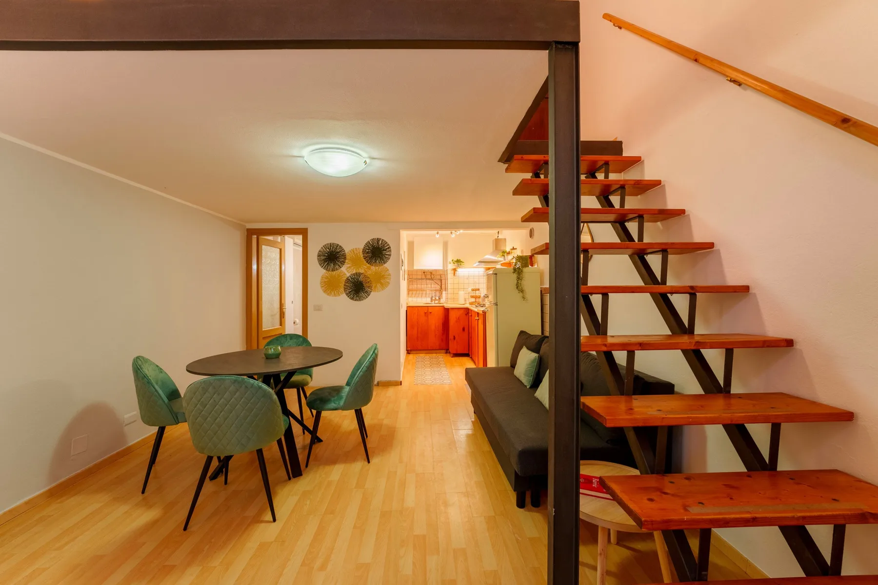 A dining area with a round table sits beside an open staircase and a kitchen.