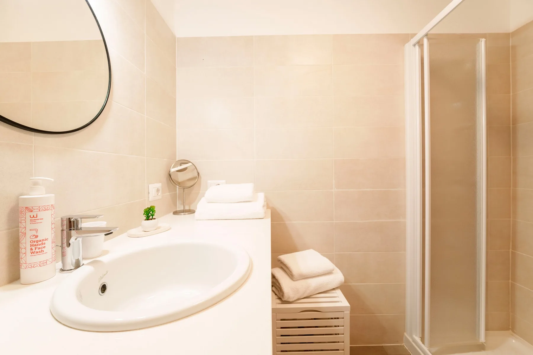 A tiled bathroom with a sink, folded towels, and a shower.
