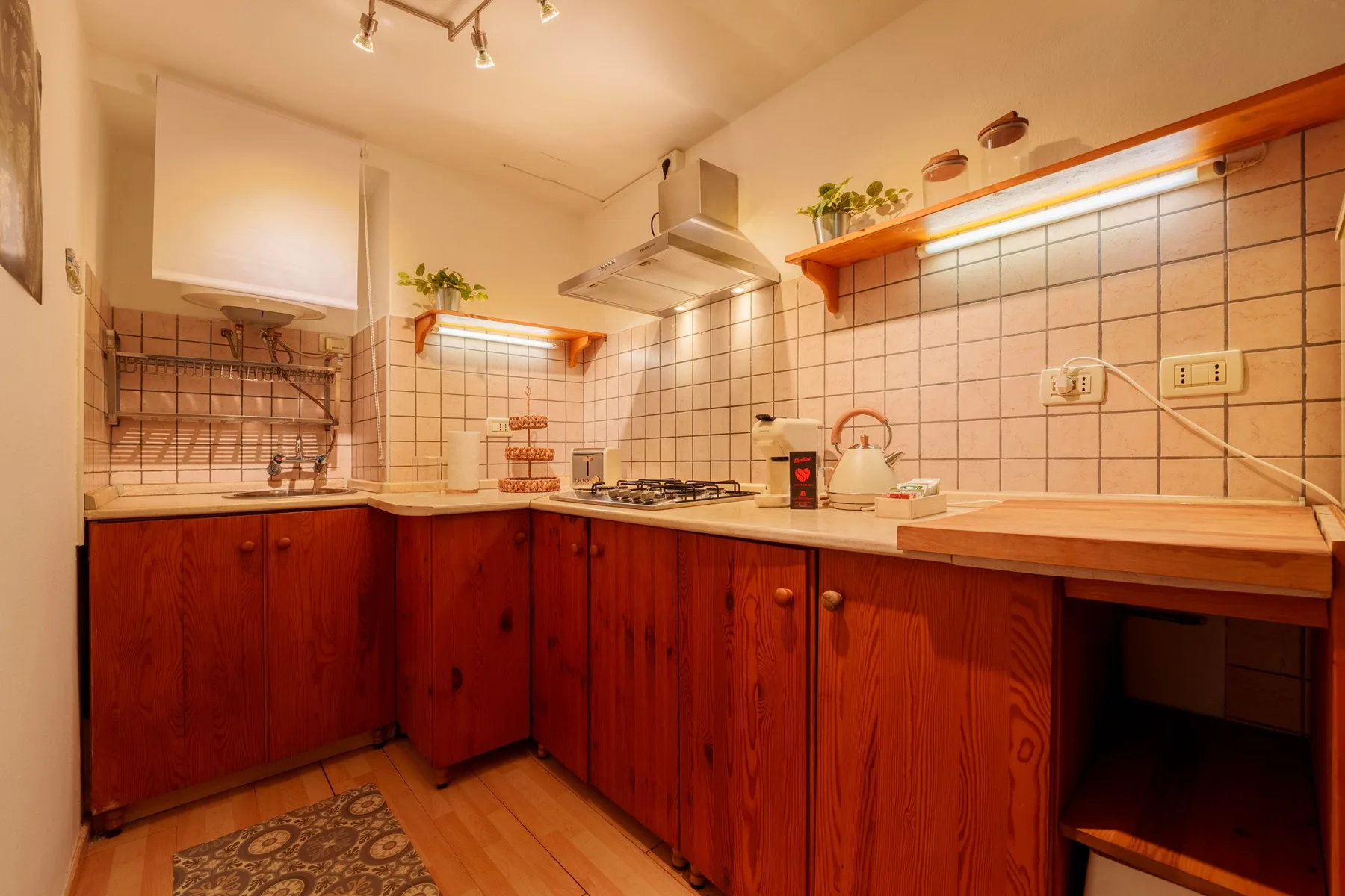 A tiled kitchen with wooden cabinets, a cooktop, and a kettle on the counter.