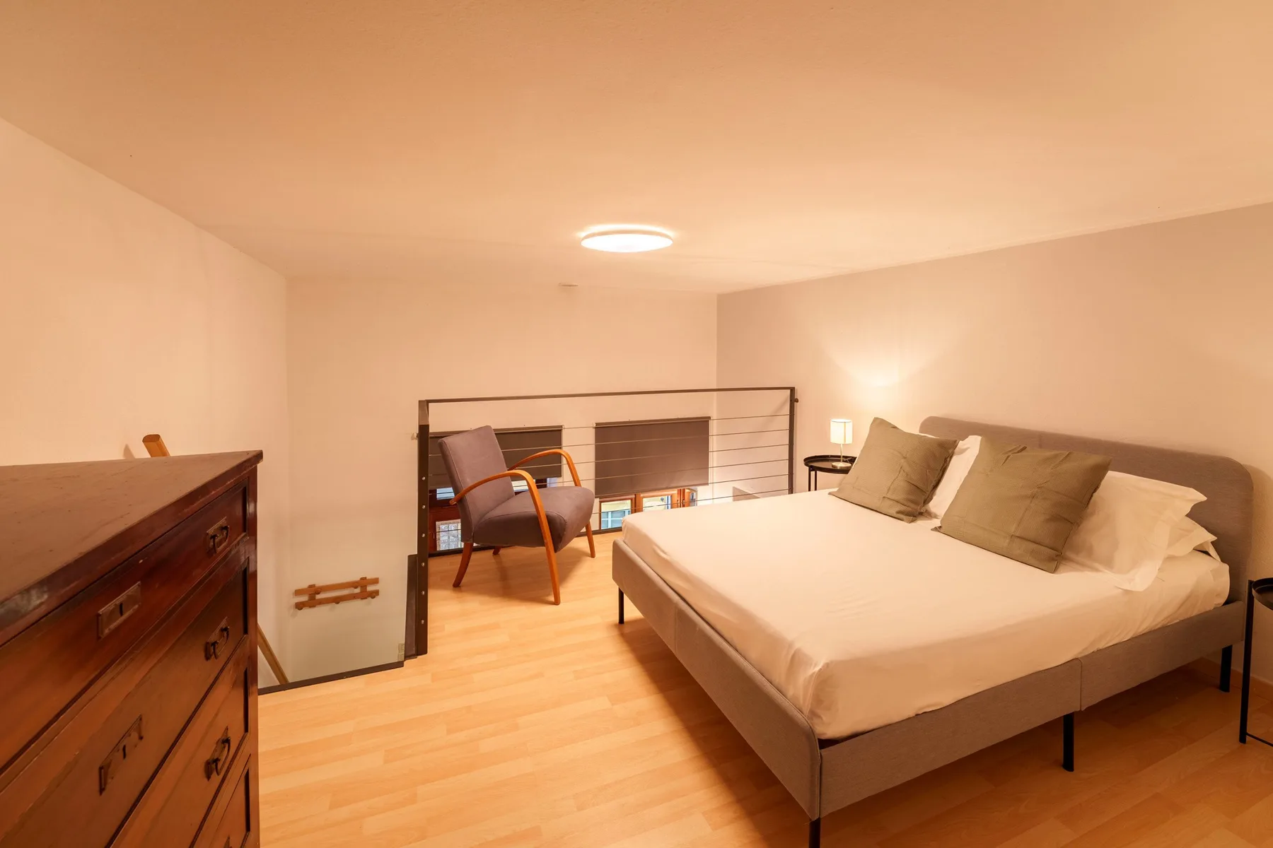A bedroom with a large bed and a chair beside a railing.