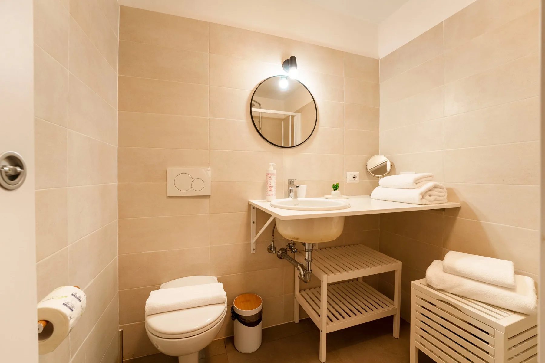 A tiled bathroom with a round mirror above the sink and a toilet nearby.