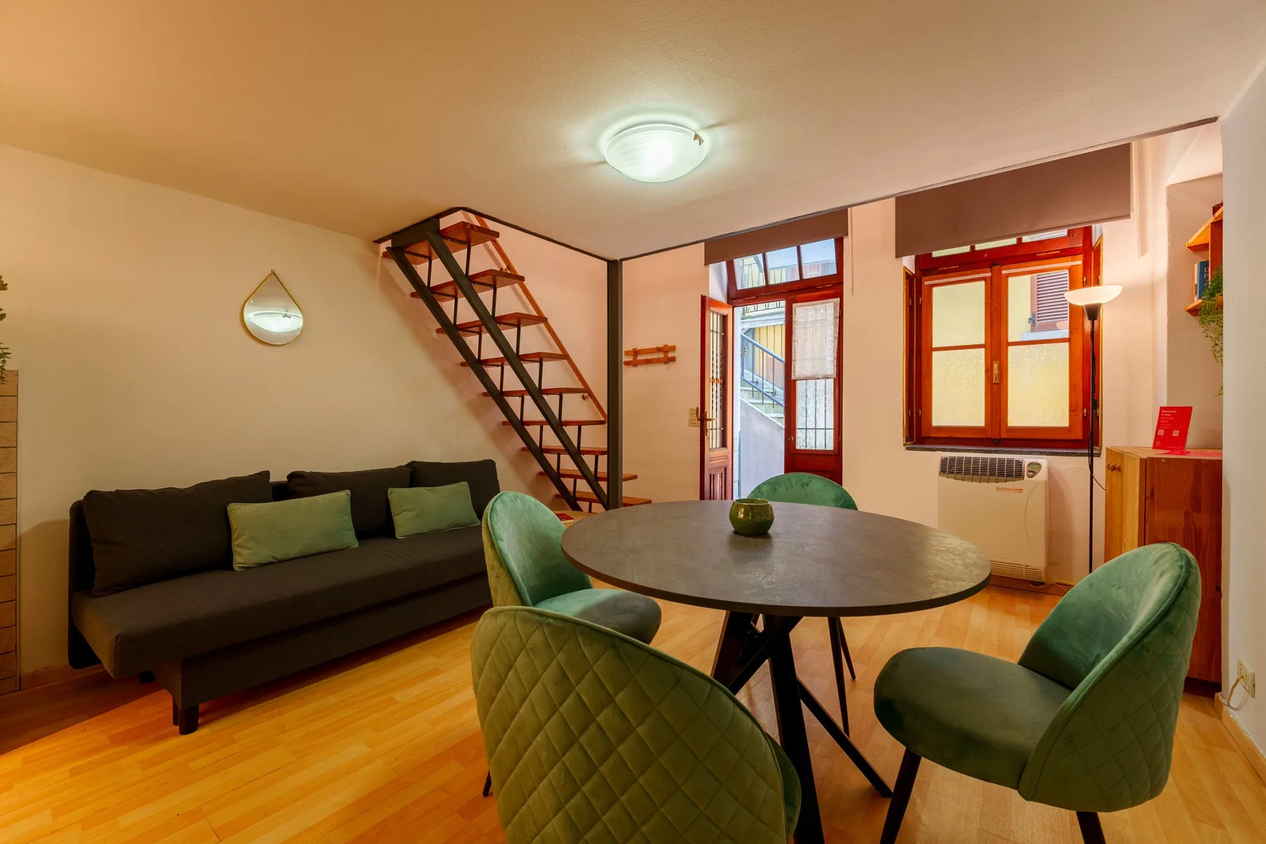 A dining area with a round table, green seating, and a dark sofa.