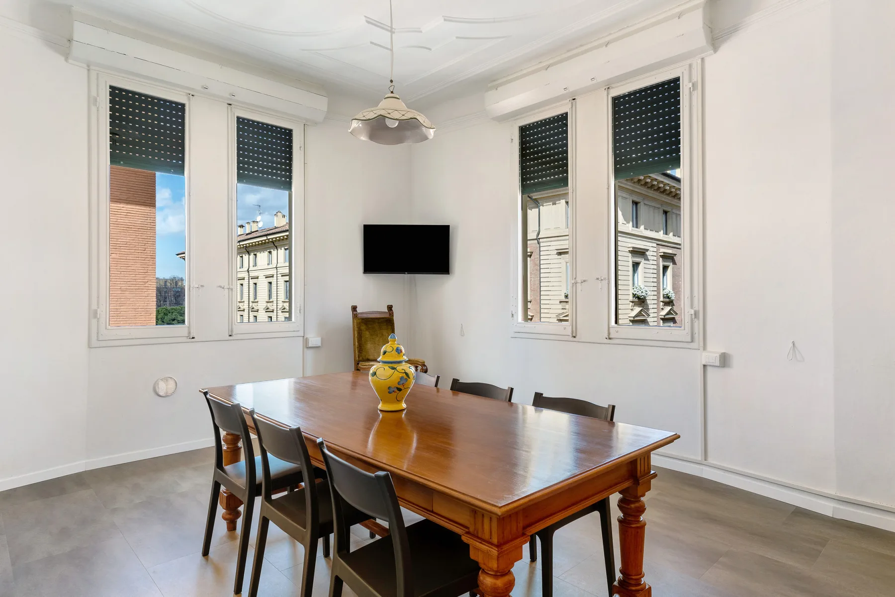 A dining room with a wooden table, chairs, and windows overlooking nearby buildings.