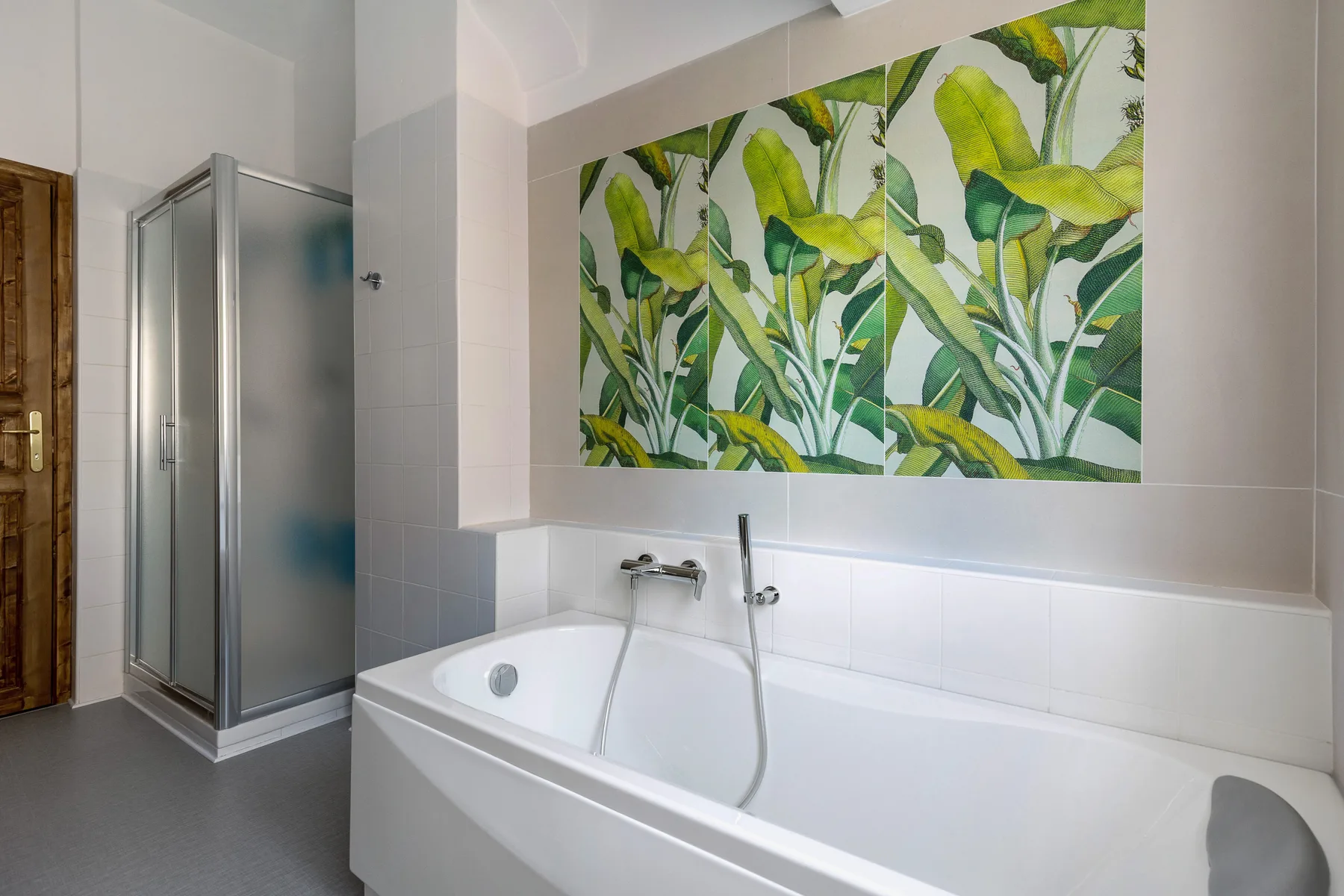 A bathroom with a bathtub, shower, and large green botanical wall mural.