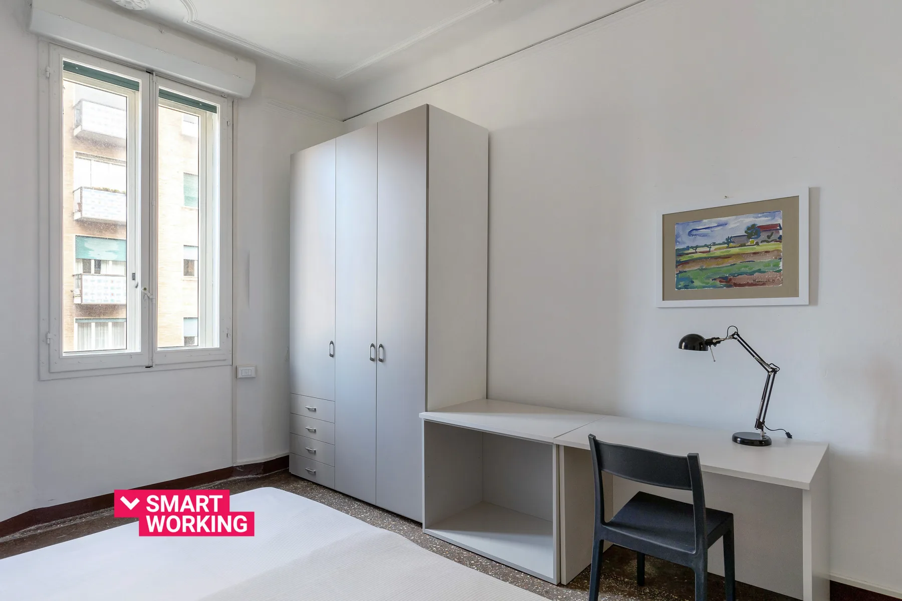 A bright study area with a desk, chair, wardrobe, and window.