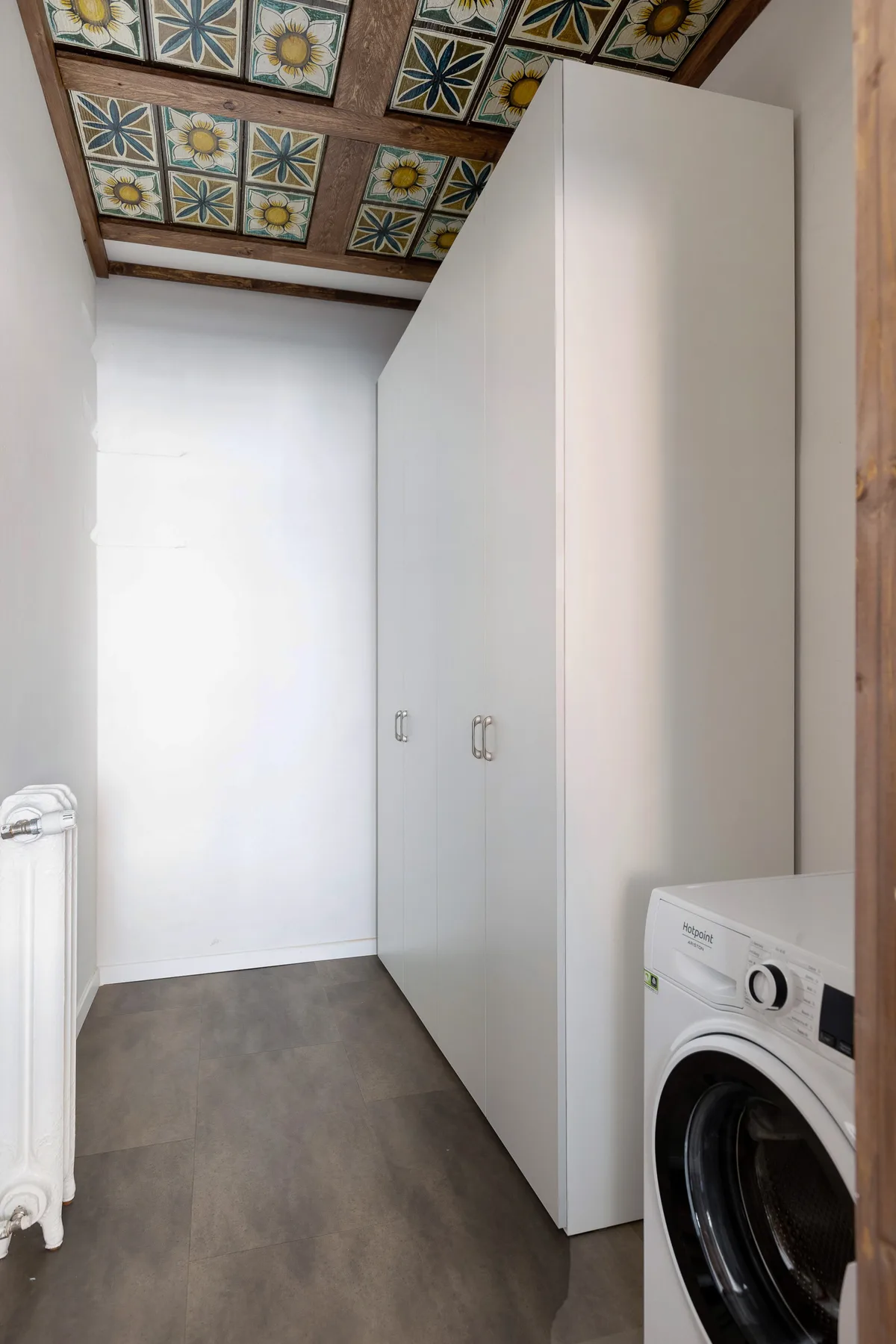 A narrow laundry area with a washing machine and tall white cabinets.