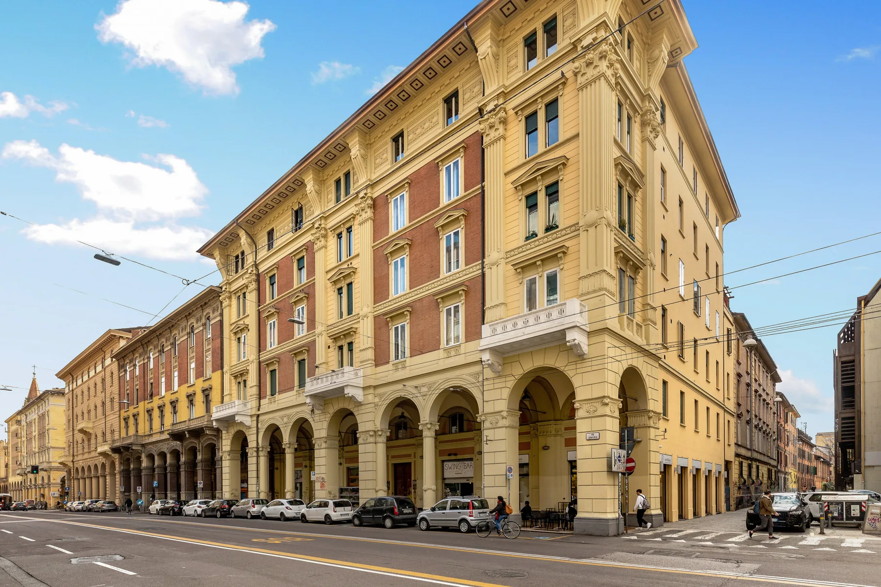 A large historic-looking building with arched ground-floor openings stands along a city street.