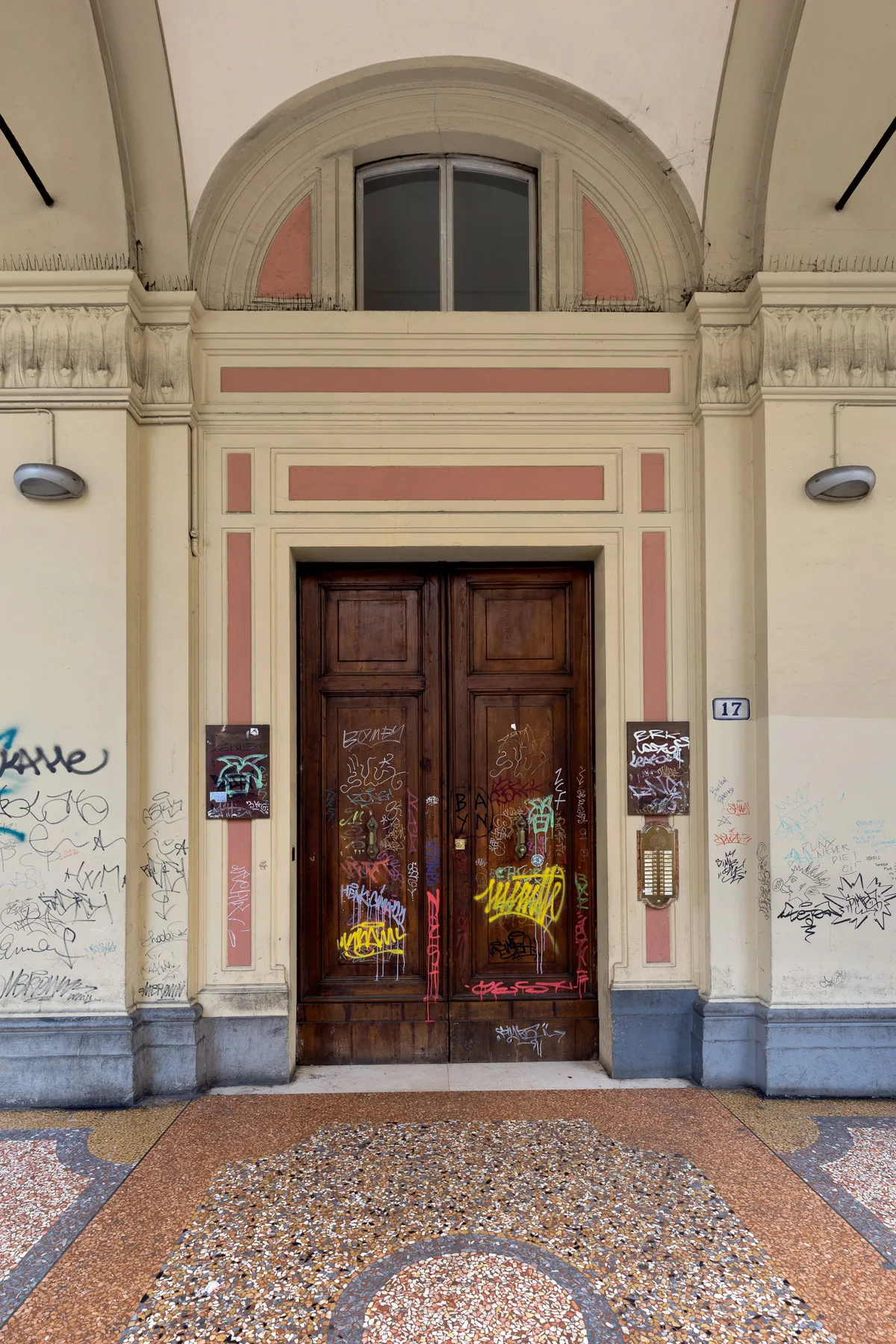 A decorated building entrance with a tall wooden double door and patterned flooring.