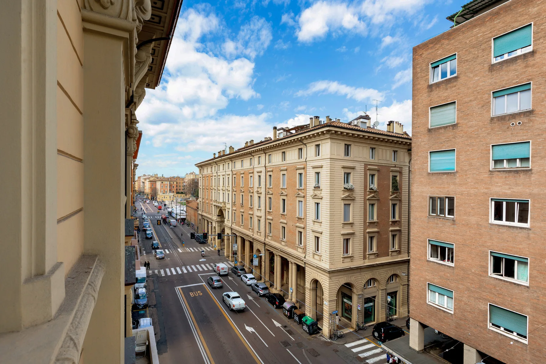 An urban street with multistory buildings and traffic beneath a partly cloudy sky.