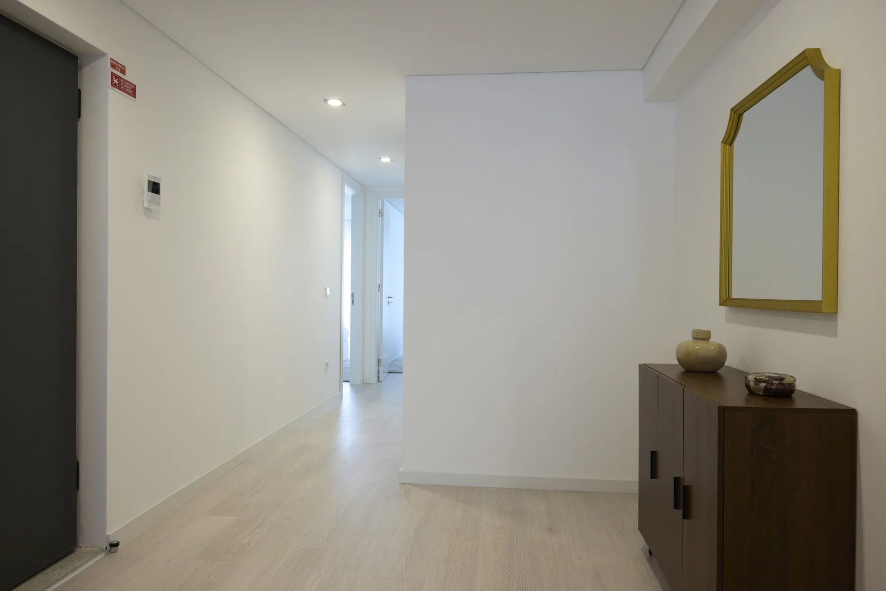 A bright apartment hallway with light flooring and a narrow console beneath a mirror.