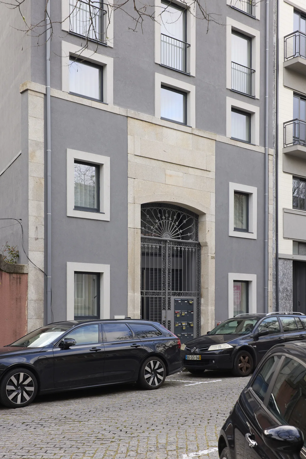 A gray apartment building facade with an arched metal entrance and parked cars.