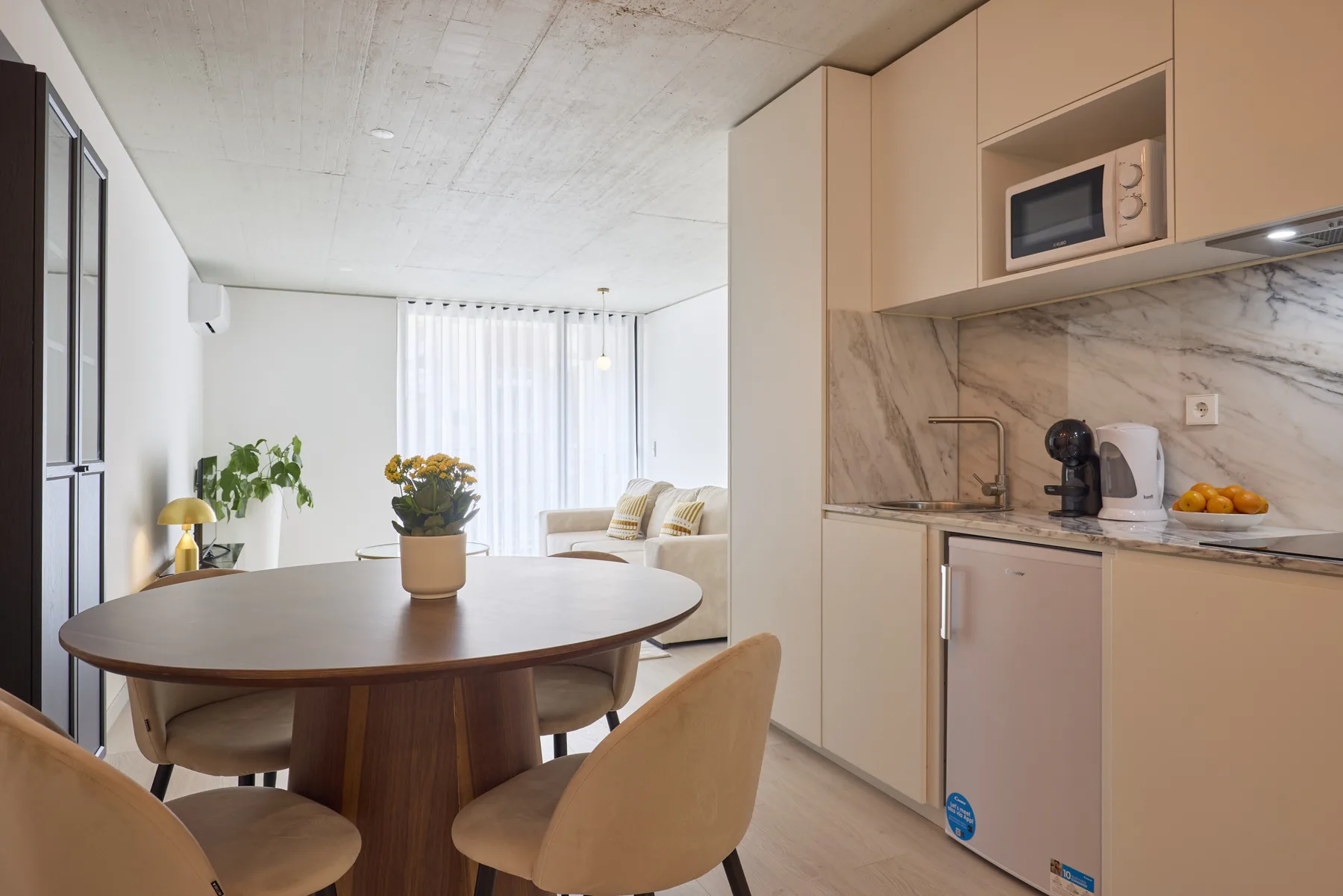 A dining area beside a compact kitchen, with a round table and light-colored seating.