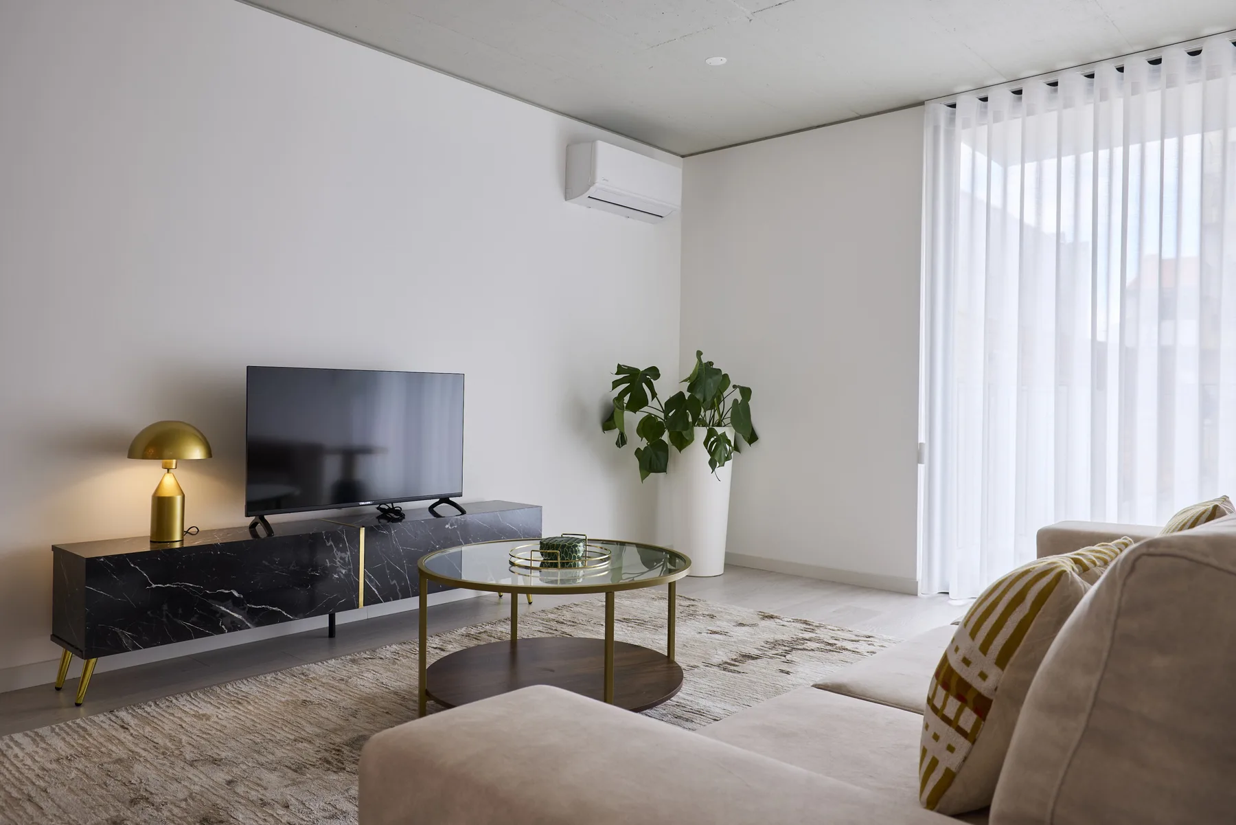 Living room with a television, coffee table, and seating beside curtained windows.