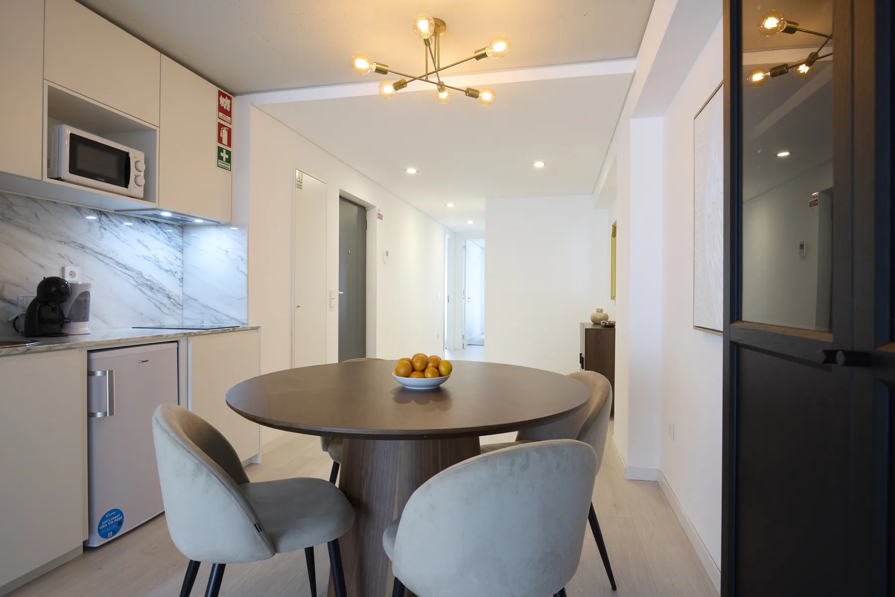 A dining area with a round table and upholstered seating beside a compact kitchen.
