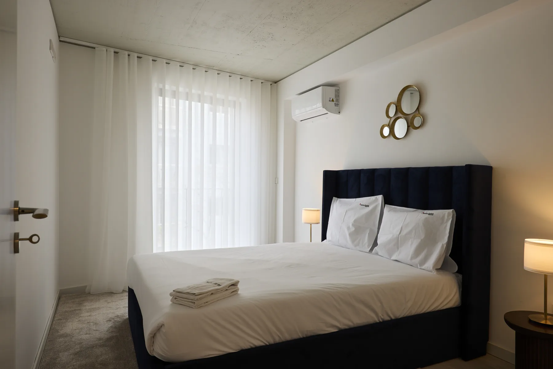A bright bedroom with a large bed, sheer curtains, and bedside lamps.
