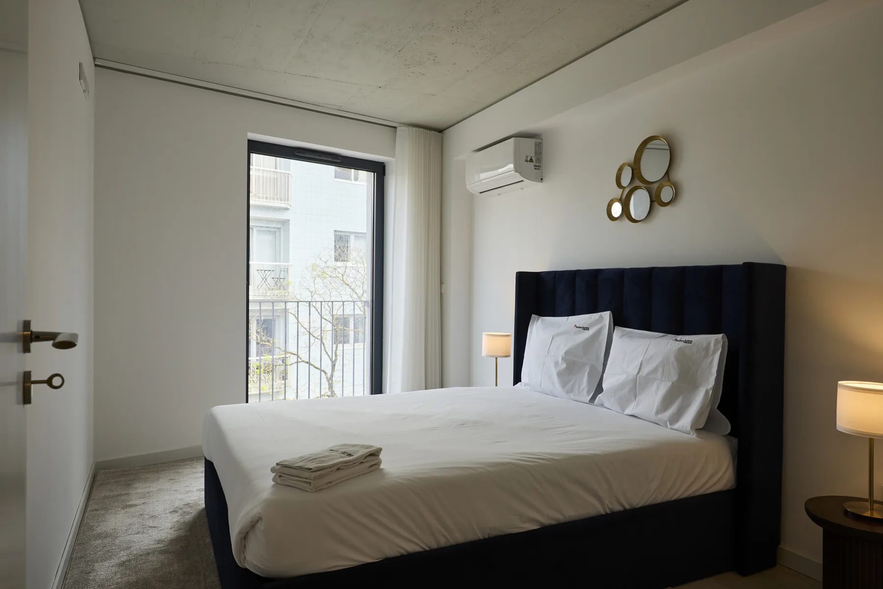 A bedroom with a neatly made bed beside a tall window.