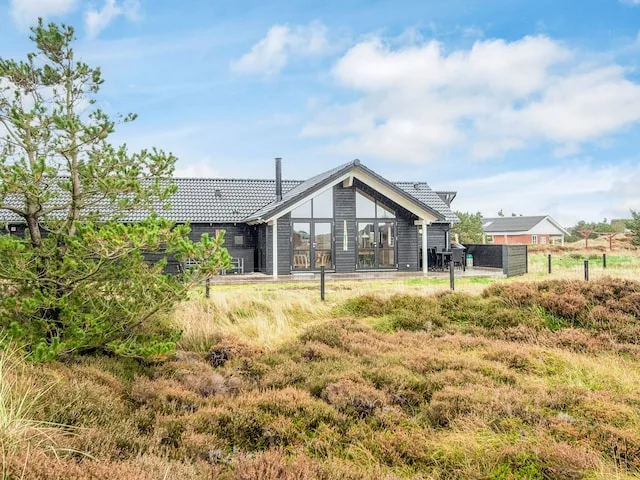 A dark-sided house with large windows stands beside grassy heathland.