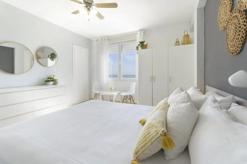 A bright bedroom with a neatly made bed and a window overlooking the sea.