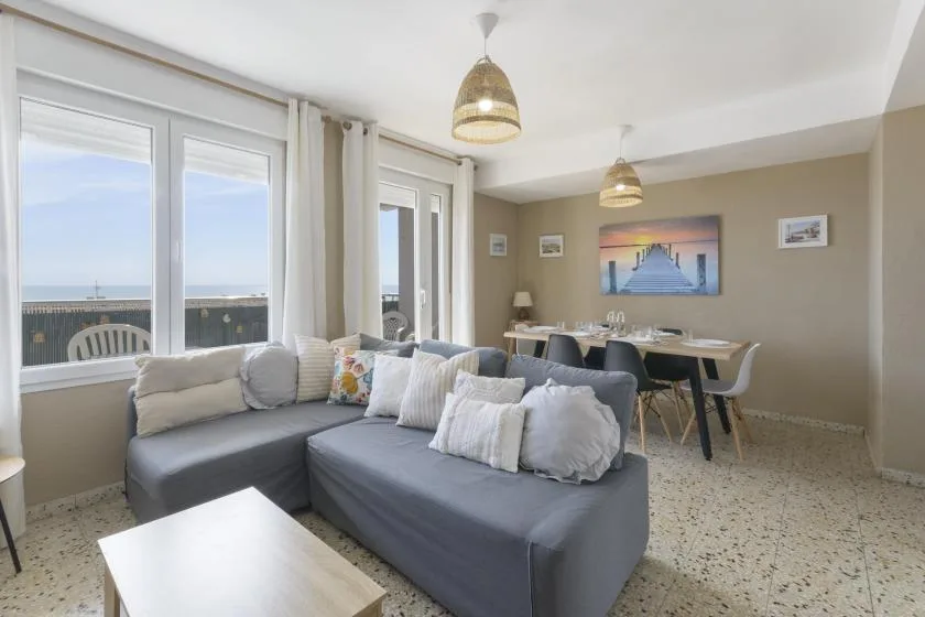 A living and dining area with gray seating, a dining table, and large windows.
