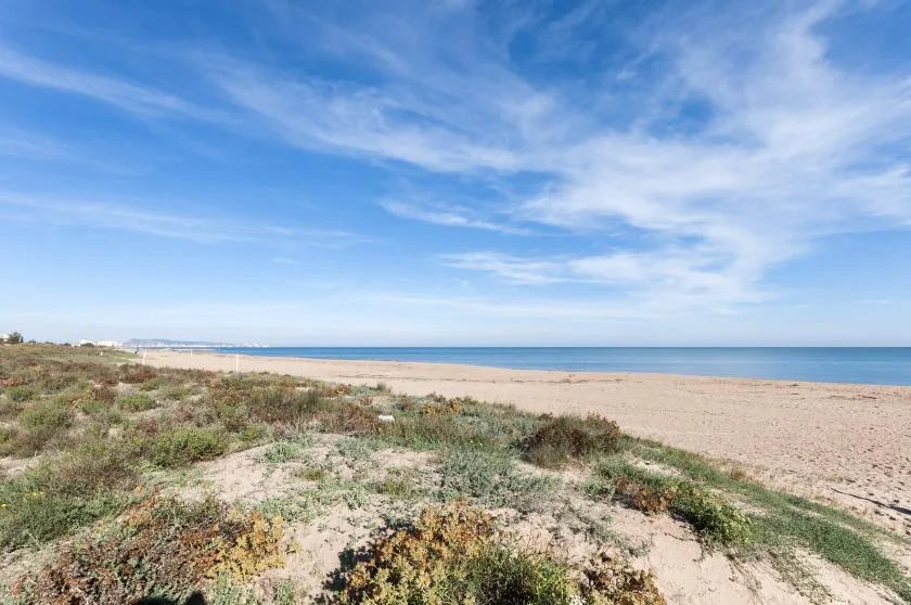 A sandy beach stretches along the calm blue sea beneath a partly cloudy sky.