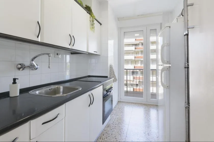A bright kitchen with white cabinets, a dark countertop, and glass doors at the far end.