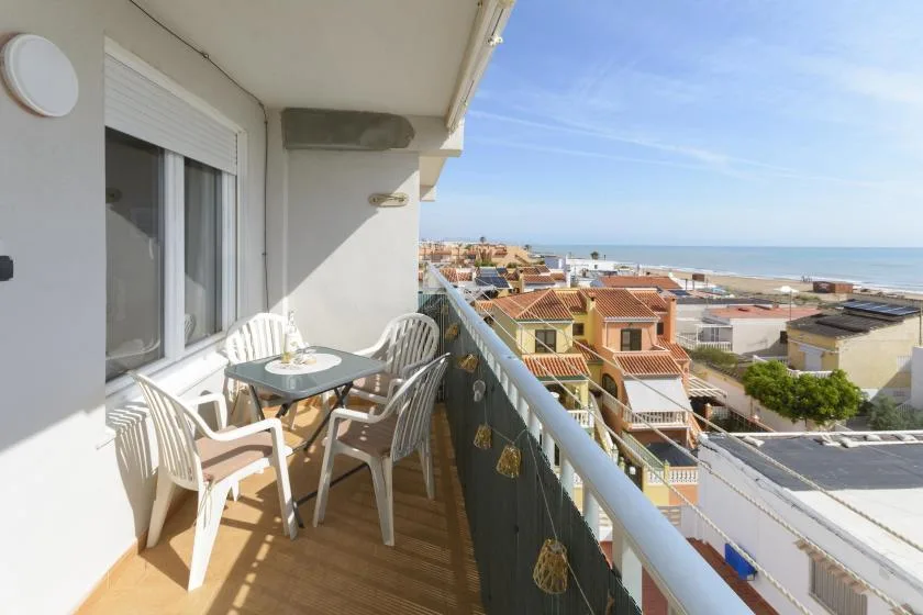 A balcony with outdoor seating overlooks nearby rooftops and the sea.
