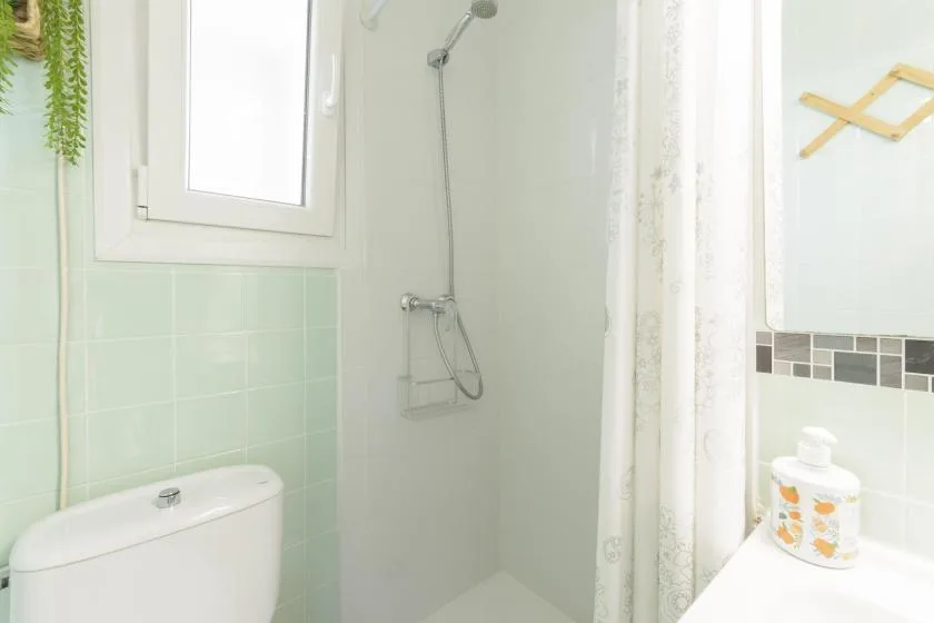 A bright bathroom with a shower, toilet, and window.