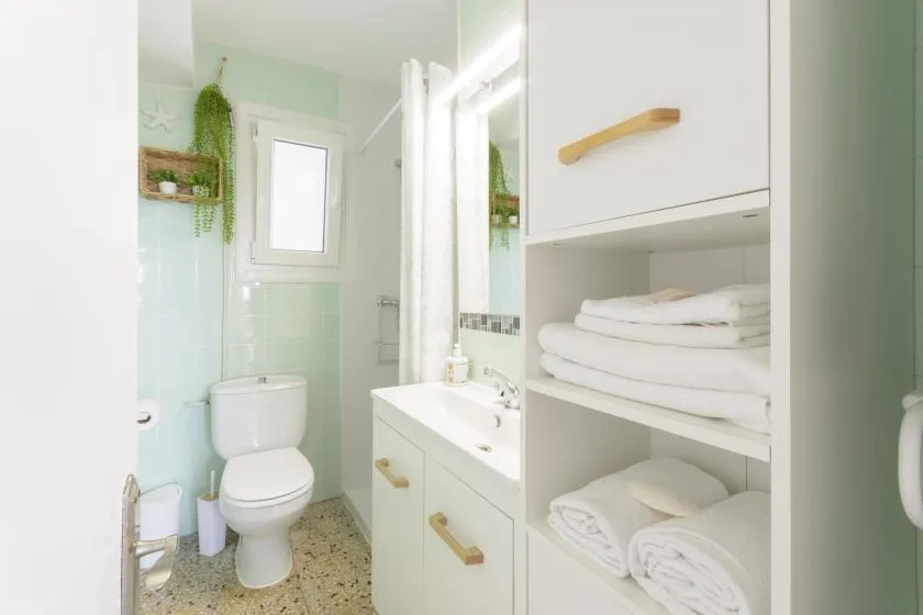 A bright bathroom with a sink, toilet, and open towel shelves.